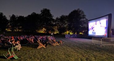 Personnes assises dans l'herbe pour regarder un film projeté sur un écran